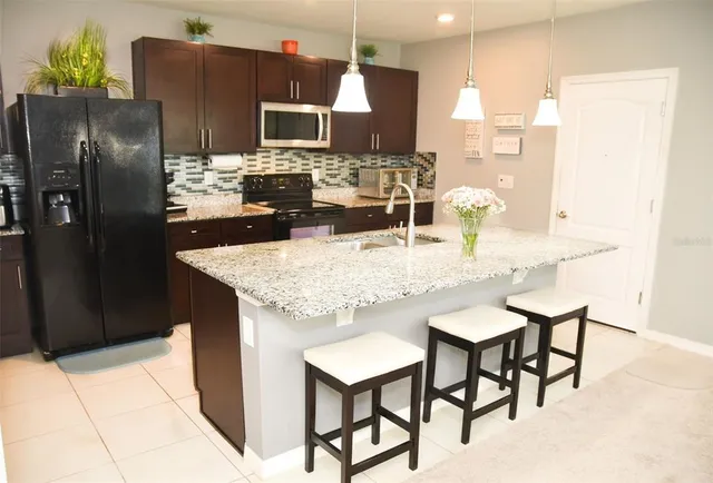 a kitchen with stainless steel appliances kitchen island granite countertop a refrigerator a microwave a sink and chairs