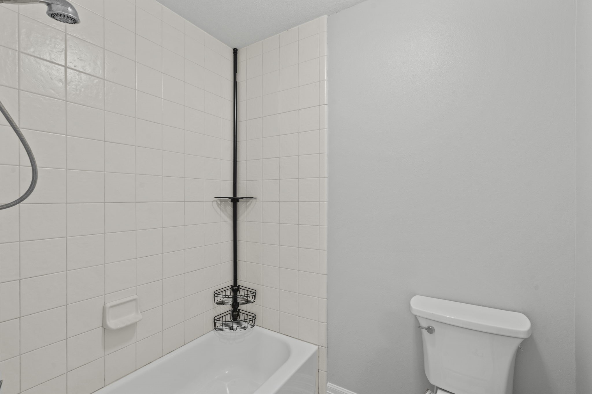 2730 Lawrence Road Kemah, TX 77565 - Photo 39 of 46 This bathroom features a clean design with white tiled walls and a bathtub-shower combo. It includes a shower caddy for storage and a standard toilet. The space is simple and functional.