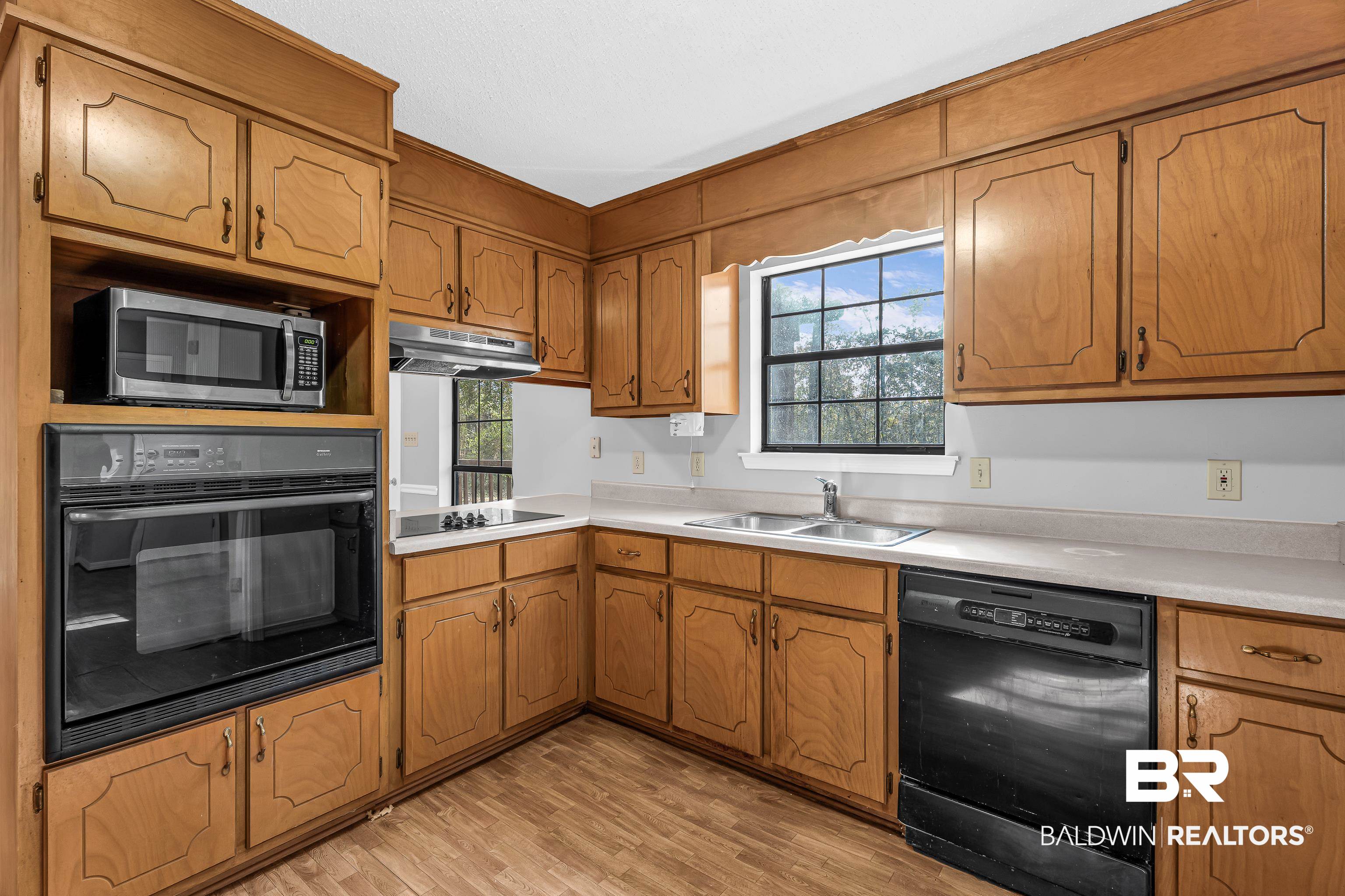 7787 Bellingrath Road Theodore, AL 36582 - Photo 15 of 36 Kitchen with black appliances, light countertops, brown cabinetry, light wood finished floors, and under cabinet range hood