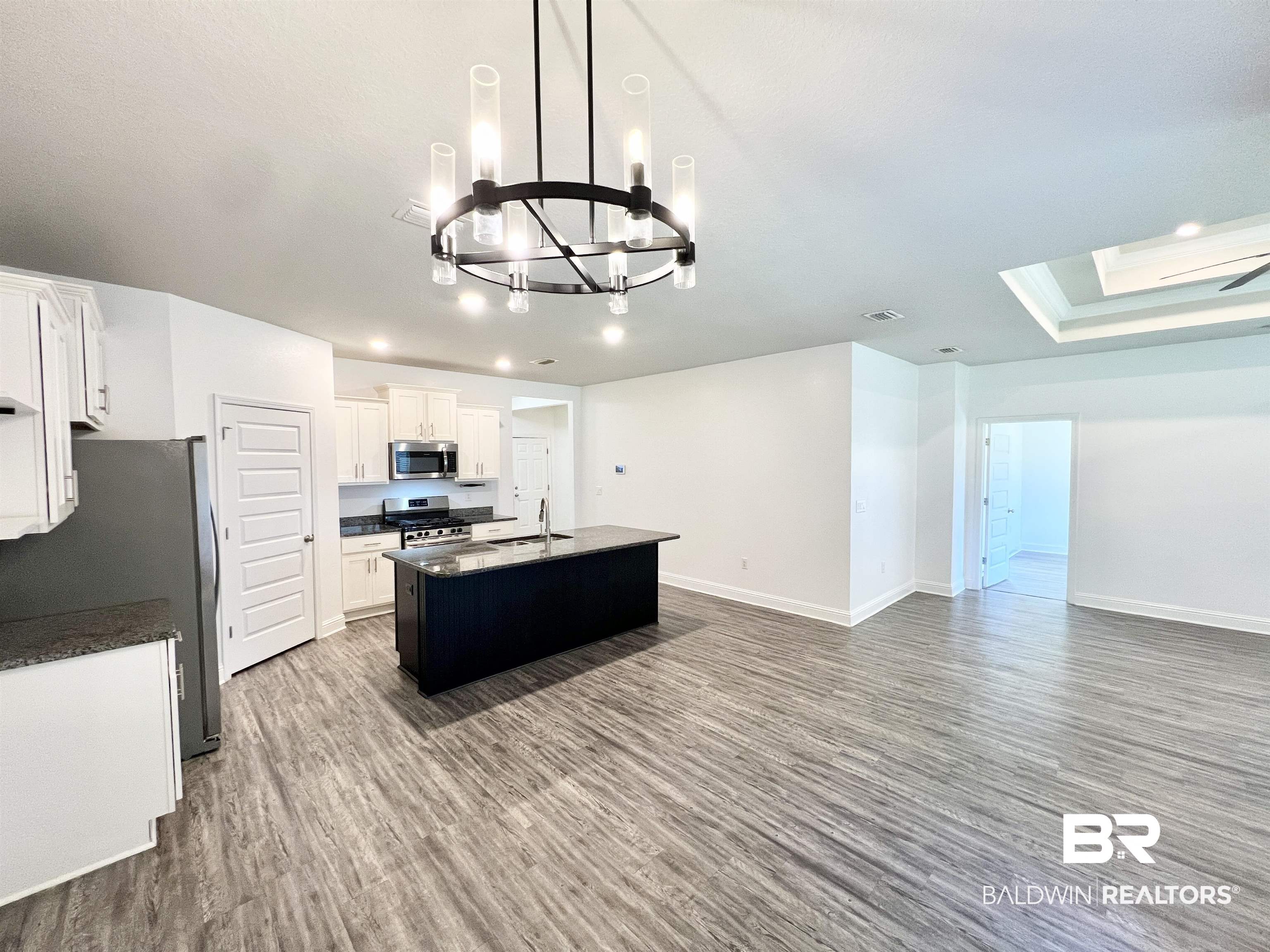 24785 Slater Mill Road Daphne, AL 36526 - Photo 11 of 46 Kitchen with white cabinets, appliances with stainless steel finishes, an inviting chandelier, a kitchen island with sink, and hardwood / wood-style flooring
