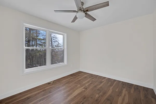 an empty room with wooden floor fan and windows