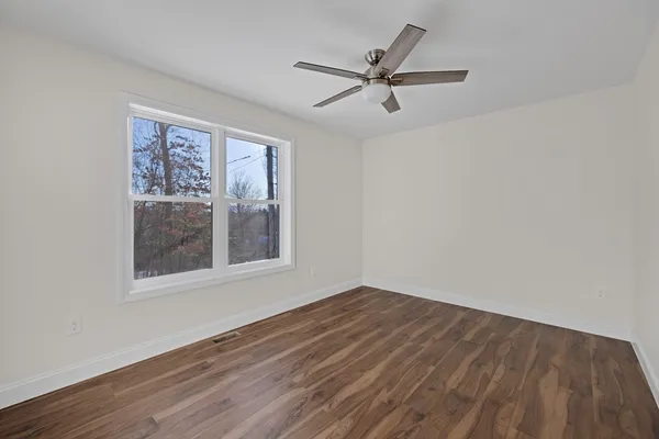 an empty room with wooden floor fan and windows