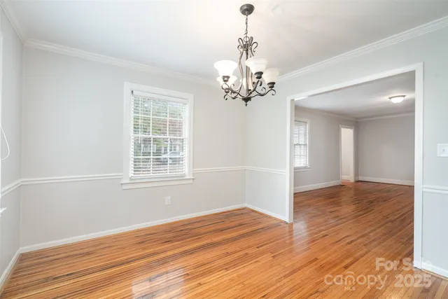 a view of empty room with wooden floor and chandelier