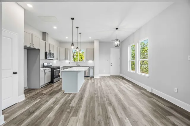 a view of a kitchen with kitchen island wooden floors appliances and a window