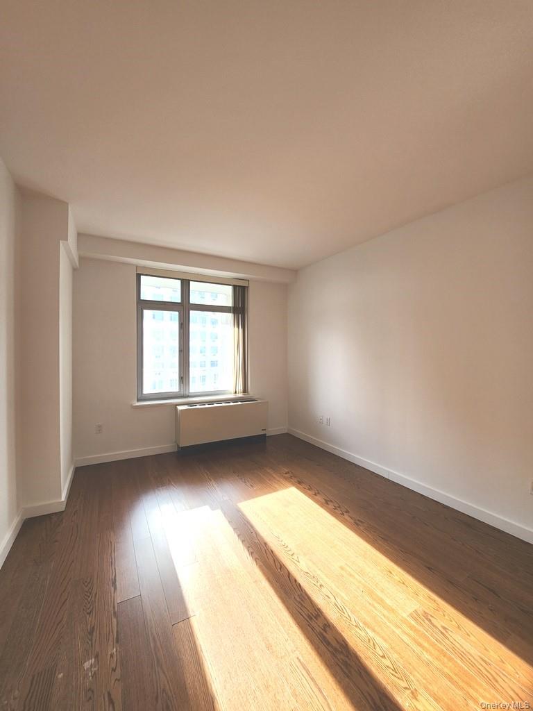 40-26 College Point Boulevard, Unit 18K Queens, NY 11354 - Photo 5 of 16 an empty room with wooden floor and windows