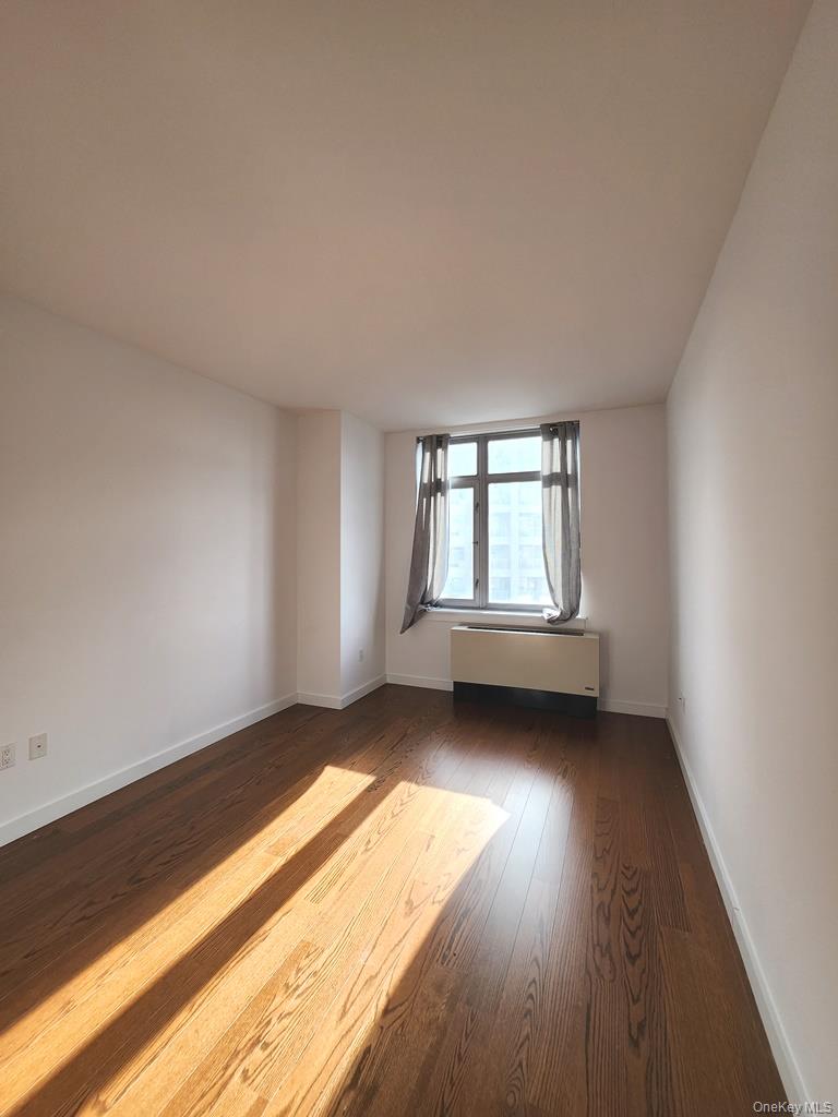 40-26 College Point Boulevard, Unit 18K Queens, NY 11354 - Photo 8 of 16 an empty room with wooden floor and windows