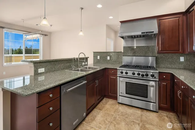 a kitchen with stainless steel appliances granite countertop a sink a stove and a wooden cabinets