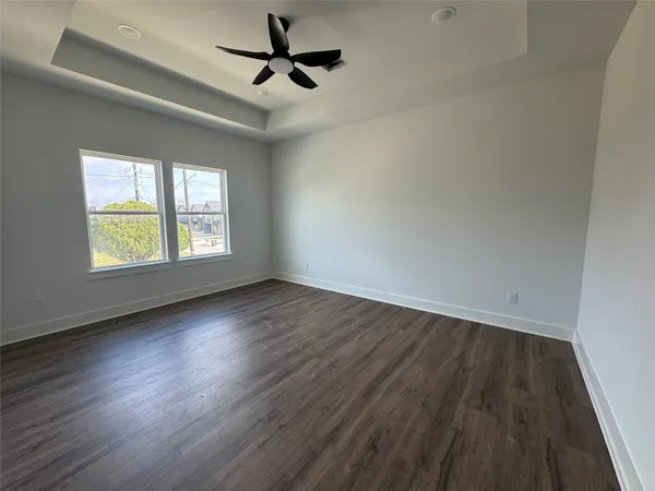an empty room with wooden floor ceiling fan and windows
