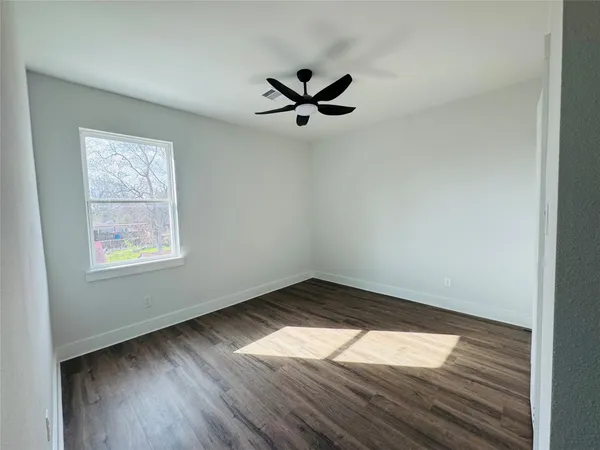 an empty room with wooden floor a ceiling fan and windows