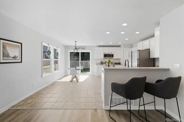 a living room with stainless steel appliances kitchen island granite countertop lots of white cabinets a dining table and chairs