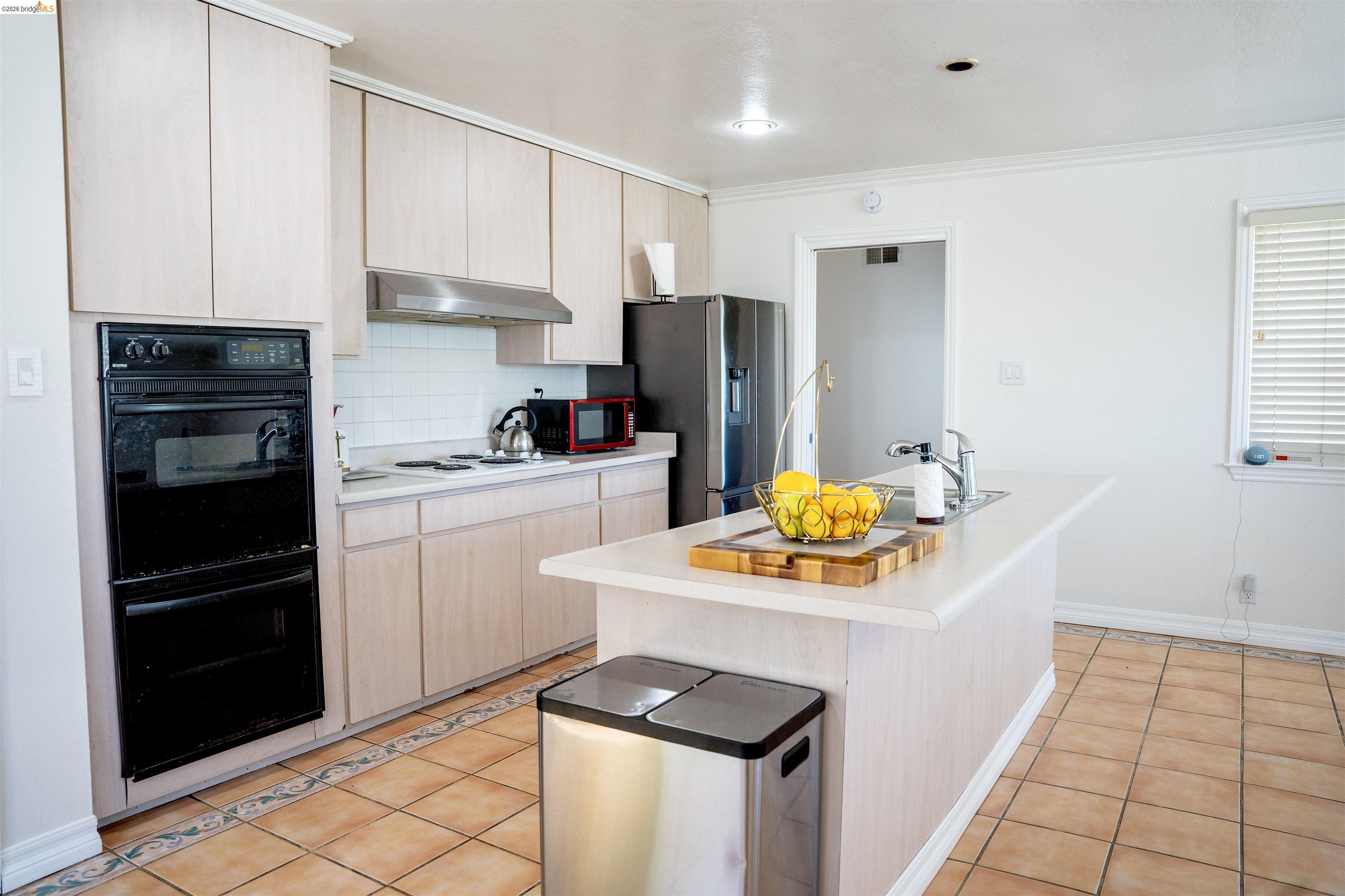 64 Washington Street Novato, CA 94947 - Photo 4 of 21 Kitchen featuring an integrated double oven, light wood-finish cabinetry, a white subway tile backsplash, a center island with sink, and terracotta-style floor tiles
