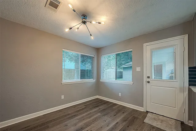 an empty room with wooden floor chandelier and windows
