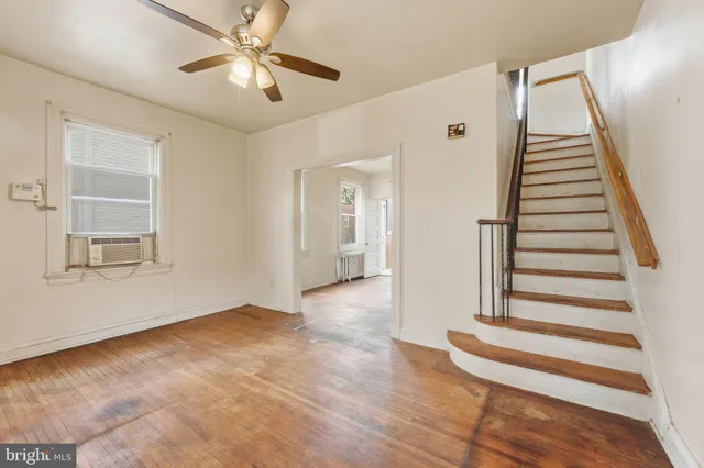 a view of an empty room with wooden floor and a ceiling fan