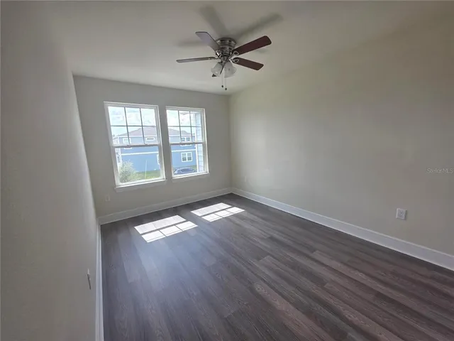 an empty room with wooden floor fan and windows