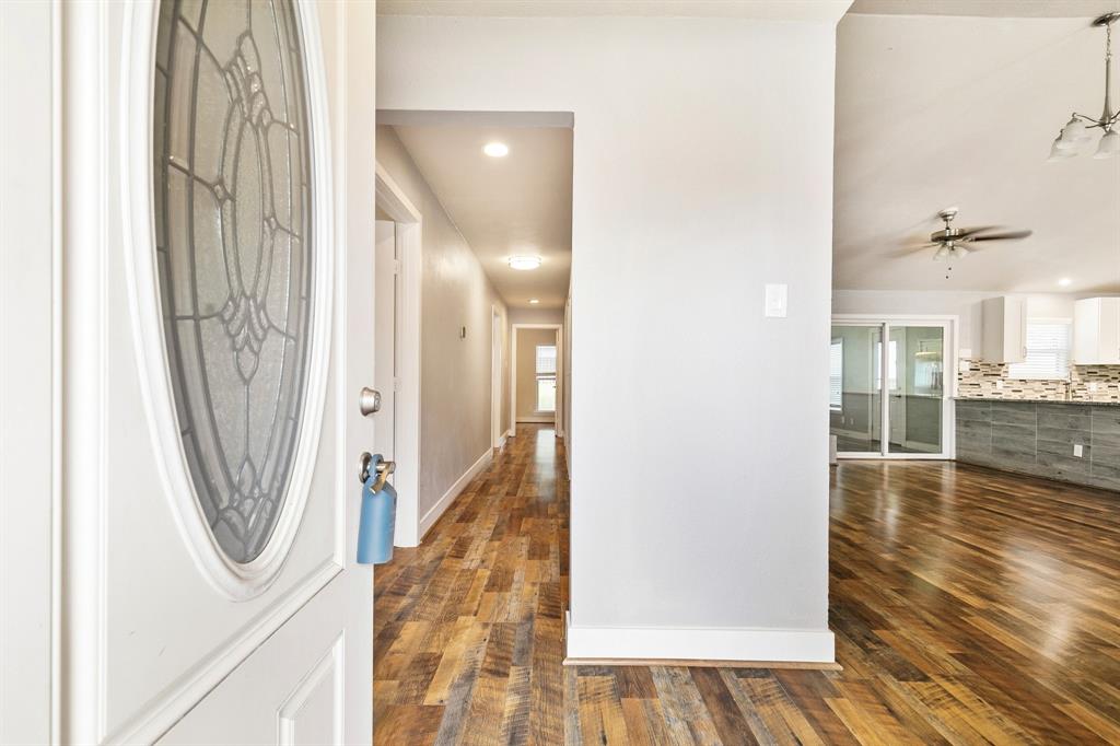 909 North Dove Road Grapevine, TX 76051 - Photo 5 of 30 Entryway featuring a decorative glass oval door, wood-finish flooring, recessed lighting, and a sightline to a kitchen with white cabinetry and a patterned tile backsplash