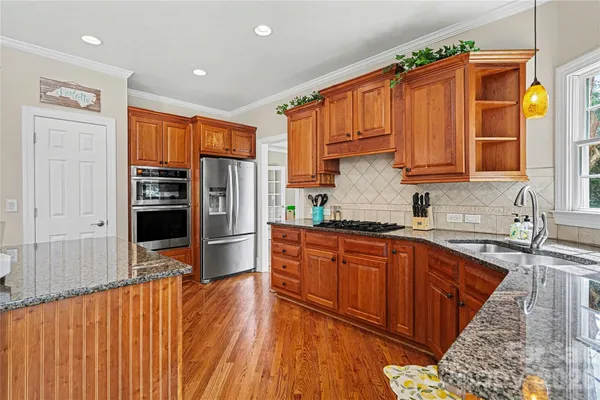 a kitchen with stainless steel appliances granite countertop a refrigerator a sink dishwasher and wooden cabinets with wooden floor