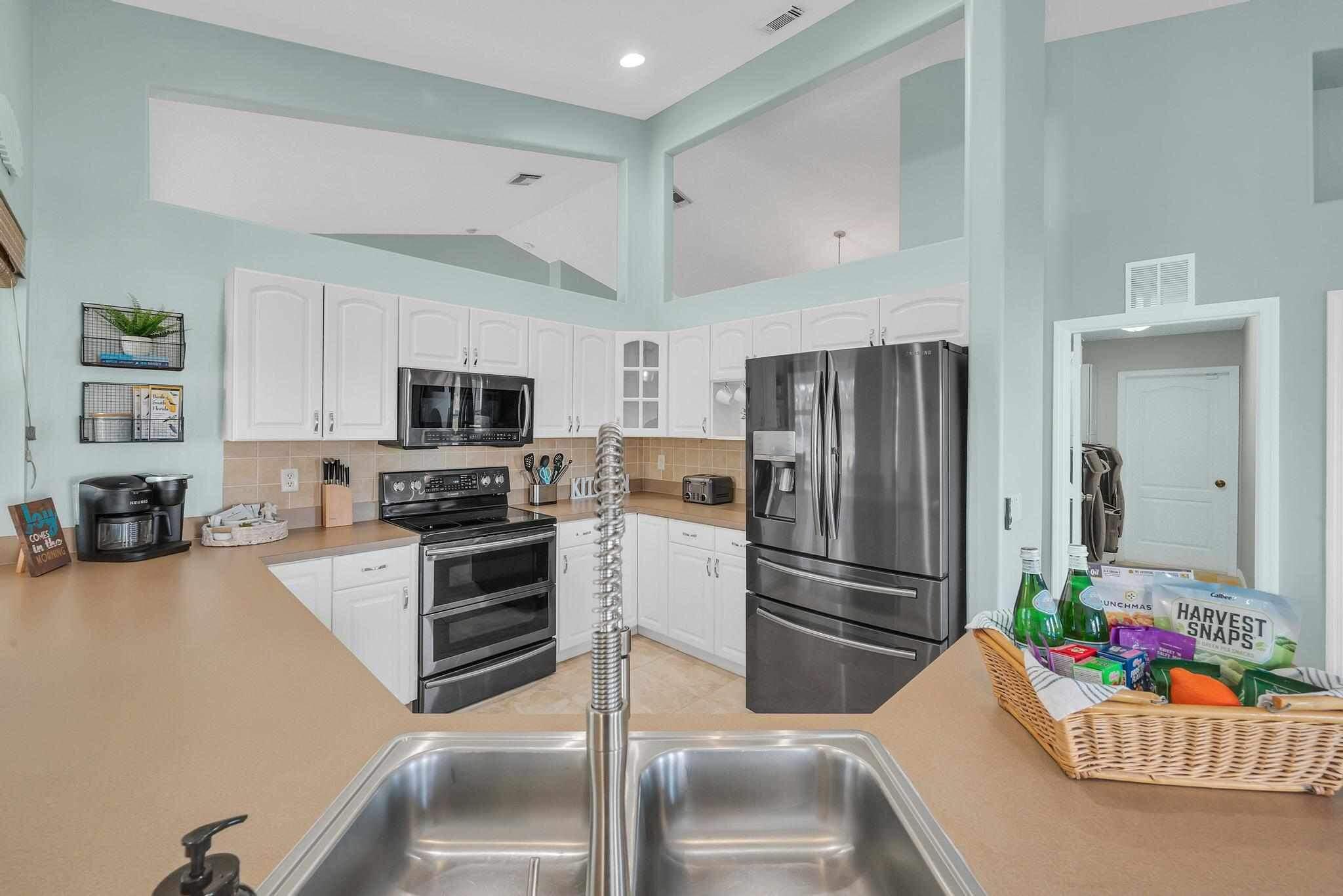 5464 Northwest Milner Drive Port St. Lucie, FL 34983 - Photo 13 of 49 a kitchen with stainless steel appliances kitchen island granite countertop a refrigerator oven a sink dishwasher and white cabinets with wooden floor