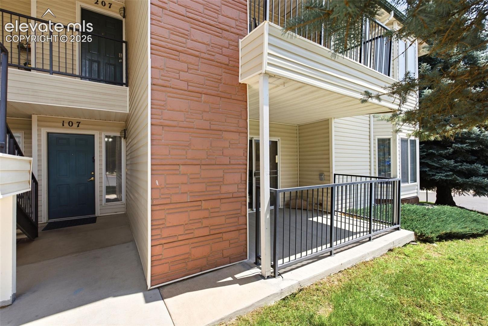 2002 Legacy Ridge View, Unit 107 Colorado Springs, CO 80910 - Photo 2 of 25 Ground-level patio with black metal railing, adjacent to a textured stone facade and light-colored siding