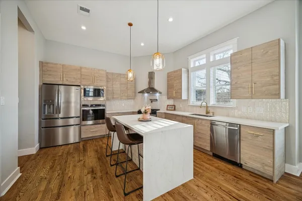 a large kitchen with stainless steel appliances a large counter top a sink a refrigerator and a window