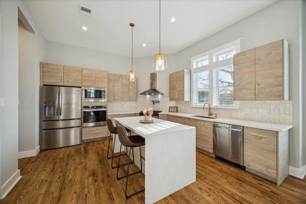 a kitchen with stainless steel appliances granite countertop a sink a stove a refrigerator and island with wooden floor