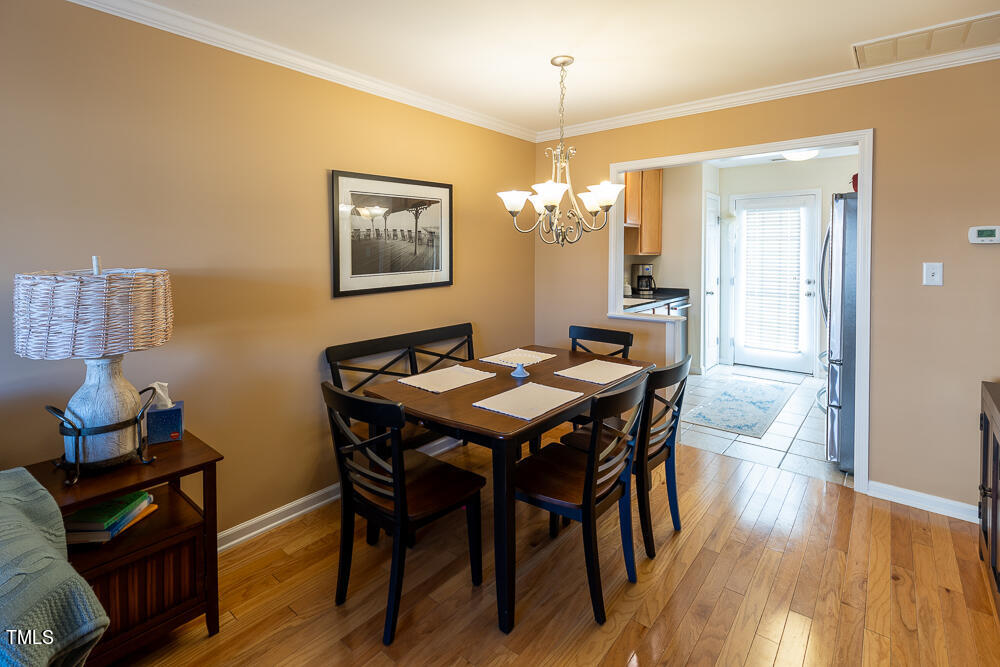 9803 Layla Avenue Raleigh, NC 27617 - Photo 8 of 30 a dining room with wooden floor a chandelier a wooden table and chairs