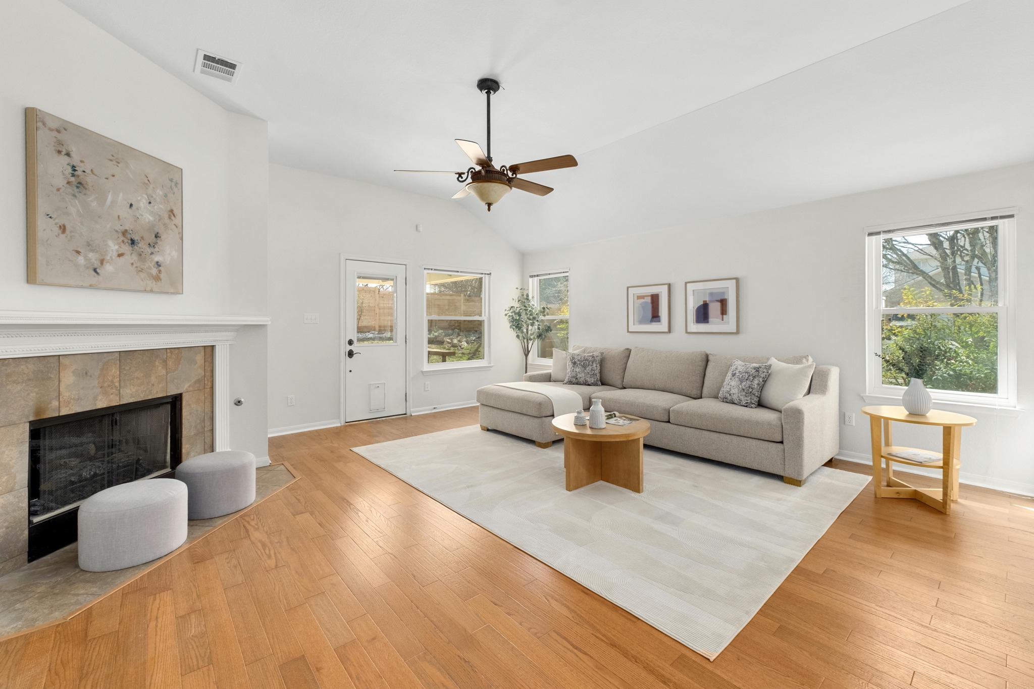 The living room stretches across the back of the home, offering a spacious gathering area with a high ceiling and a corner fireplace that naturally draws the room together