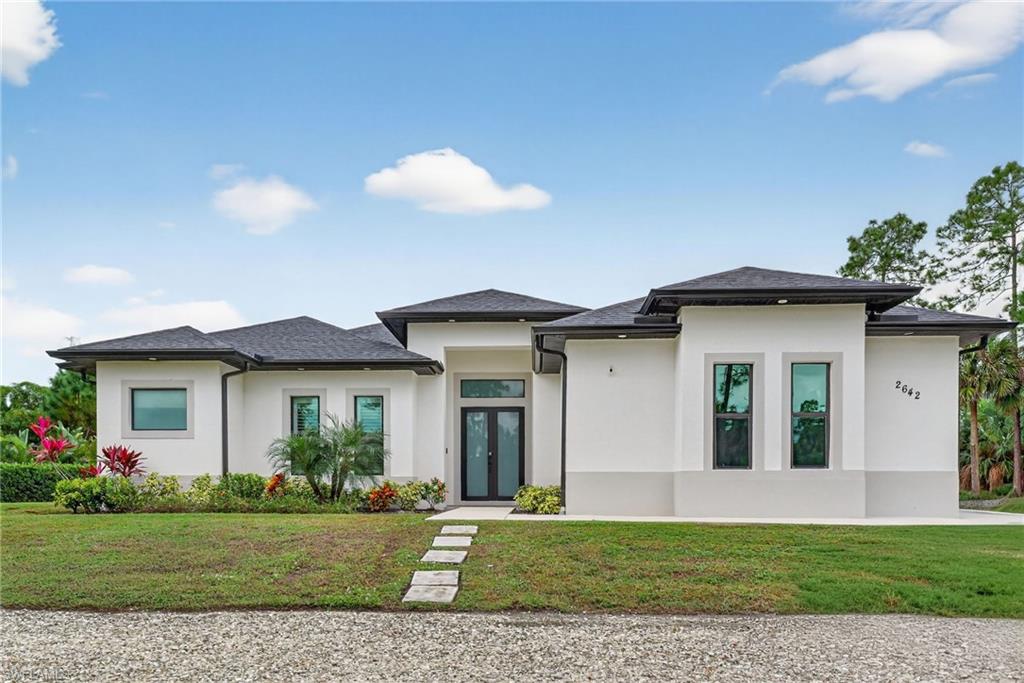 a view of a white house with a big yard and potted plants