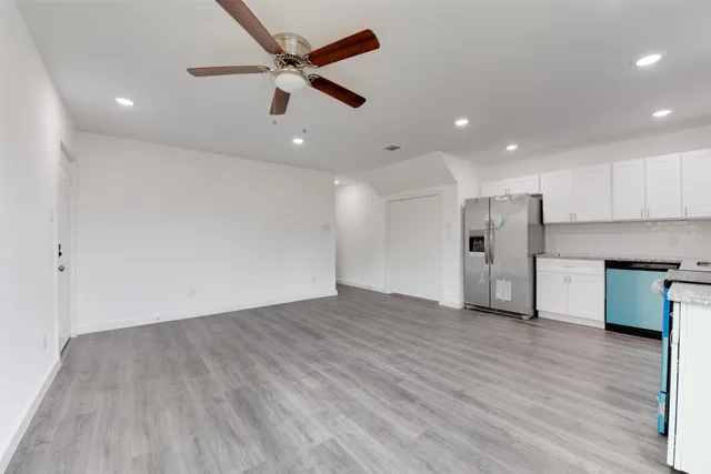 an empty room with stainless steel appliances kitchen island hardwood floor and a ceiling fan
