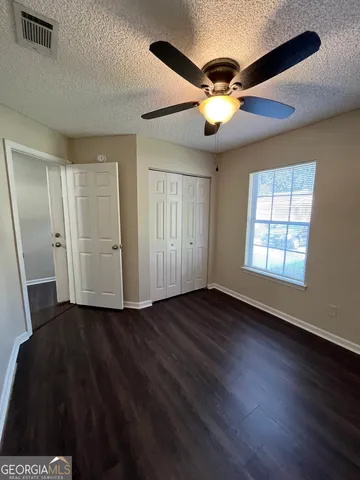 a view of an empty room with wooden floor and a ceiling fan