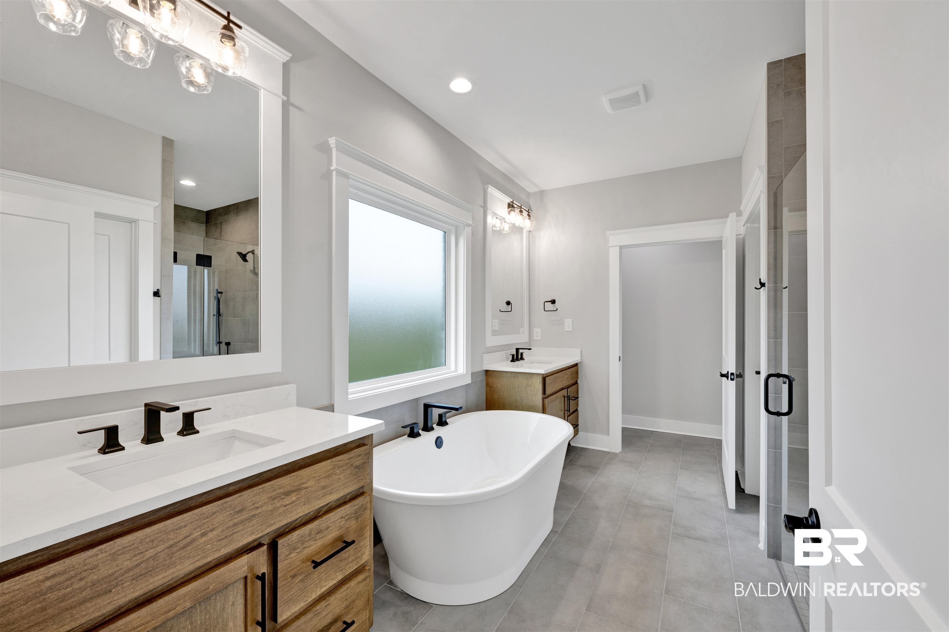 27371 Patch Pl Loop Daphne, AL 36526 - Photo 54 of 63 Bathroom featuring a freestanding soaking tub with floor-mounted fixture, dual wood-finish vanities with undermount sinks and quartz countertops, a large framed mirror, and a glass-enclosed shower with tile surround