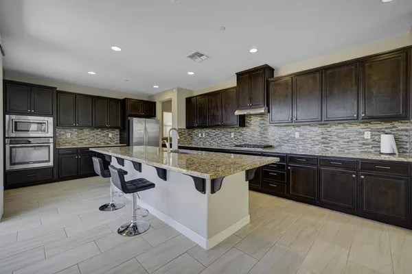 a kitchen with kitchen island granite countertop stainless steel appliances a sink a stove a refrigerator cabinets and chairs