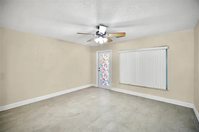 an empty room with chandelier fan and windows
