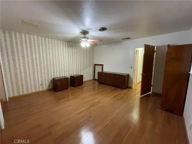 a view of an empty room with wooden floor and a ceiling fan