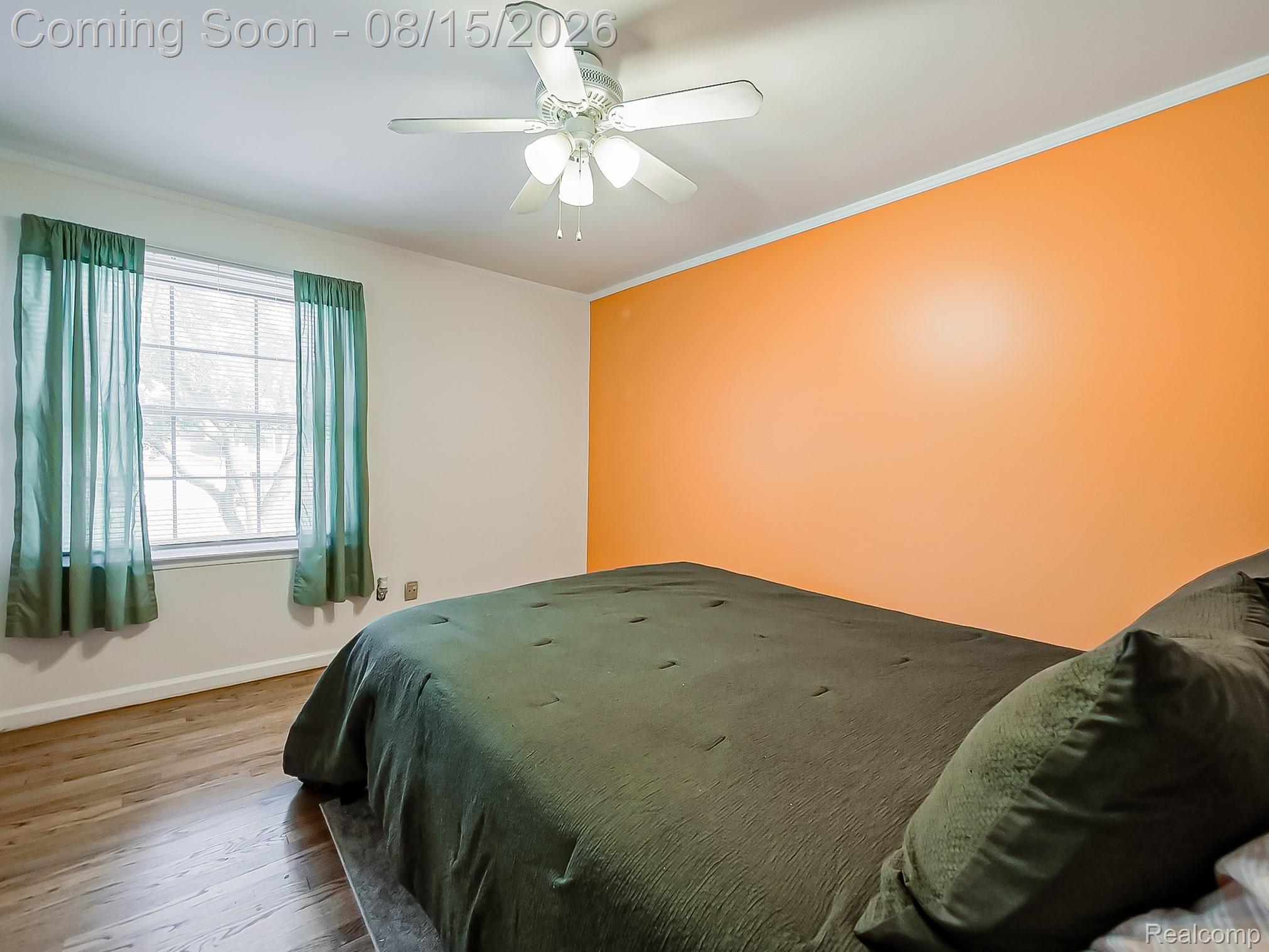 21131 Harvard Road Southfield, MI 48076 - Photo 11 of 33 Spacious bedroom featuring warm orange accent wall, wood-finish flooring, large multi-pane window with green curtains, and ceiling fan with integrated lighting