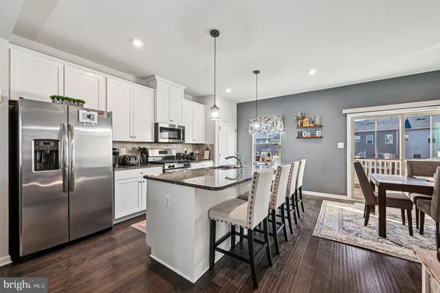 a kitchen with stainless steel appliances granite countertop a dining table chairs refrigerator and microwave