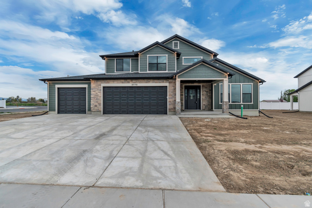 View of front of property featuring driveway, an attached garage, stone siding, and covered porch