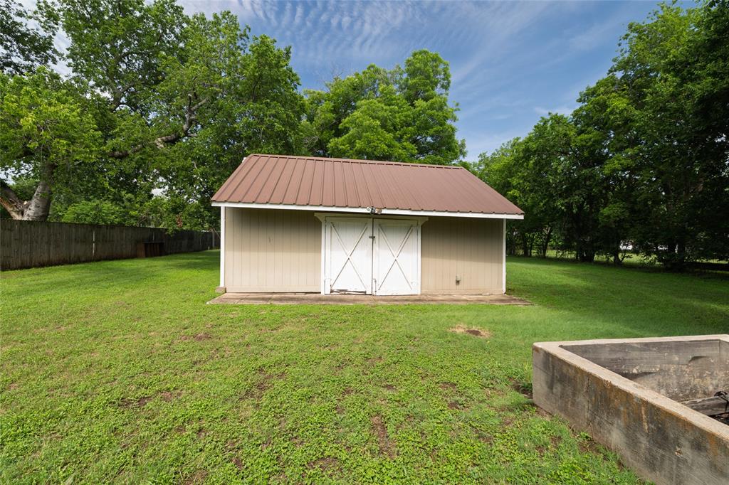 313 North Roe Street White Settlement, TX 76108 - Photo 28 of 33 Storage shed featuring a brown metal roof, light tan siding, and white double doors with crossbuck detailing