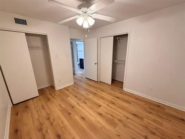 a view of an empty room with wooden floor and a ceiling fan