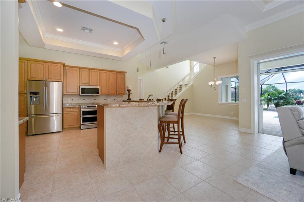 8007 Tiger Lily Drive Naples, FL 34113 - Photo 12 of 32 a kitchen with stainless steel appliances kitchen island granite countertop a refrigerator a stove a sink a dining table and chairs with wooden floor