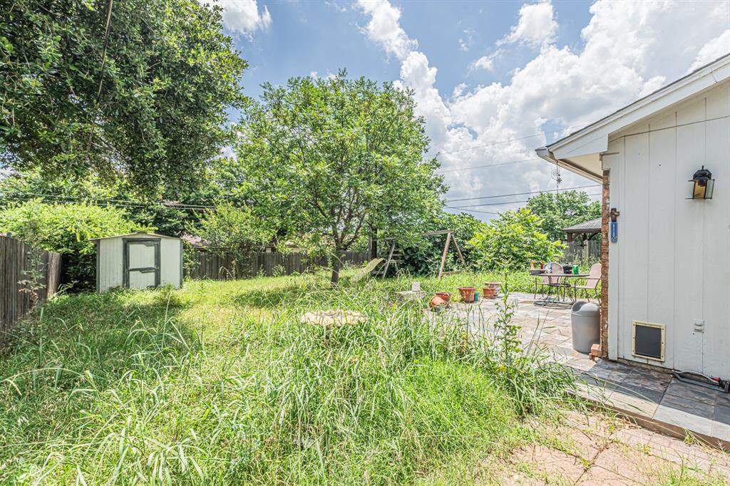 6504 Johnnie Street Watauga, TX 76148 - Photo 21 of 23 Expansive backyard featuring a stone patio, mature trees, wood fencing, and a storage shed