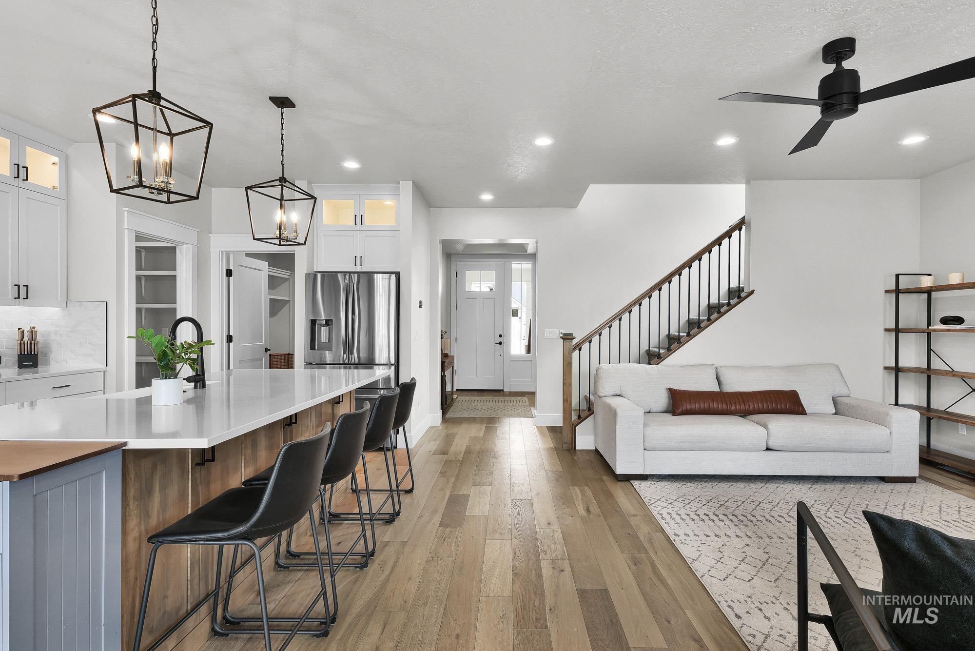 5676 East Zaffre Ridge Street Boise, ID 83716 - Photo 19 of 50 Open-concept living space featuring wood-finish flooring, a kitchen island with seating, stainless steel refrigerator, white cabinetry, and a staircase with dark metal balusters