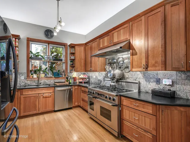 a kitchen with stainless steel appliances granite countertop wooden cabinets a sink dishwasher a stove and a refrigerator with wooden floor