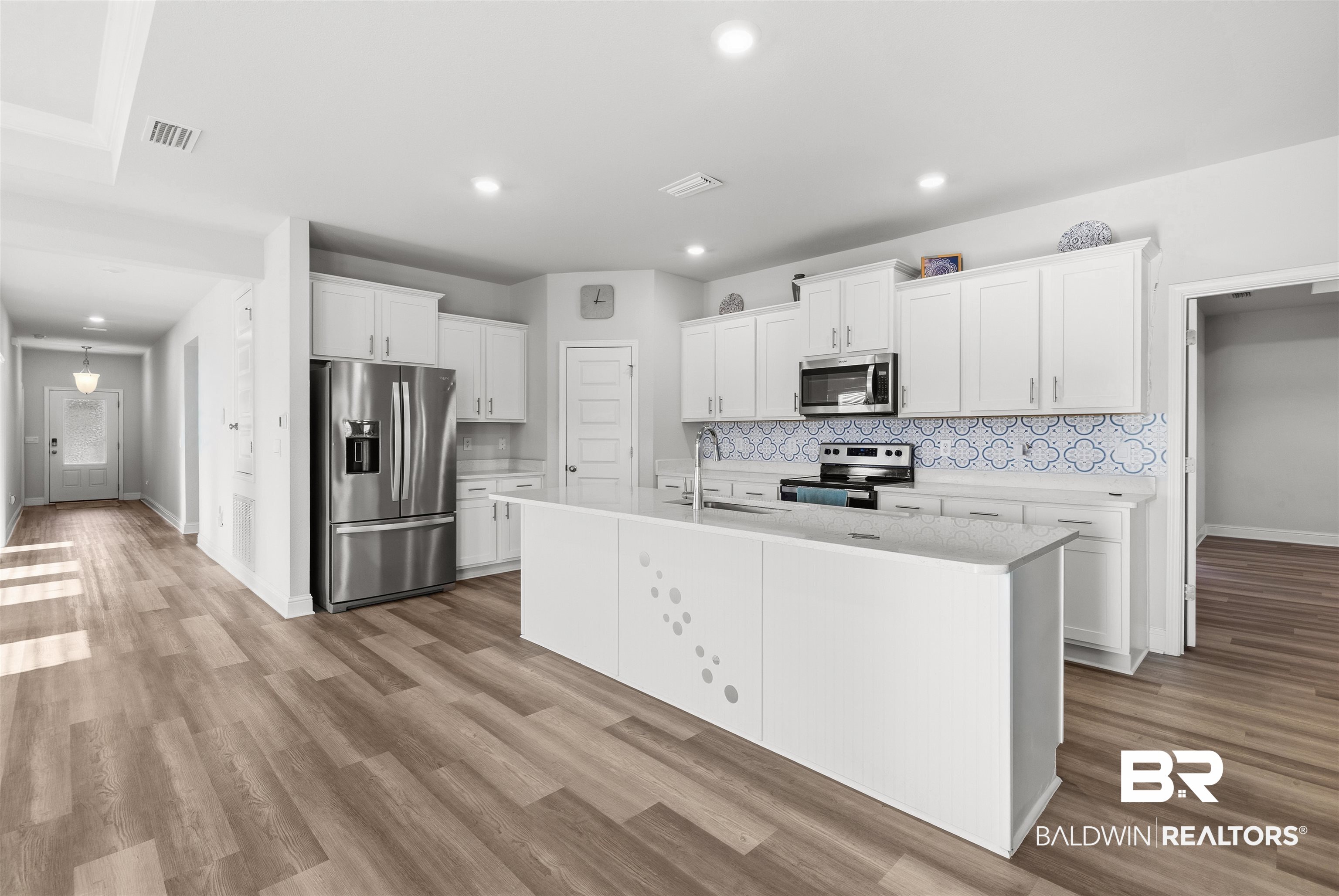 485 Shepard Street Gulf Shores, AL 36542 - Photo 15 of 53 Kitchen with white cabinets, appliances with stainless steel finishes, light wood finished floors, an island with sink, and tasteful backsplash