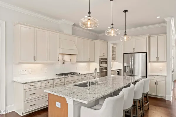 a kitchen with stainless steel appliances granite countertop a sink a stove a refrigerator and white cabinets with wooden floor