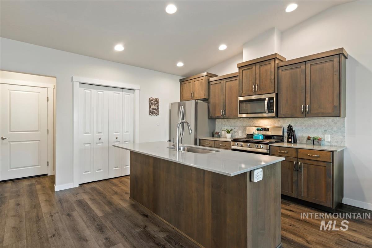 193 West Haniken Street Meridian, ID 83642 - Photo 8 of 27 Kitchen featuring stainless steel appliances, a kitchen island with sink, backsplash, dark wood finish cabinetry, and dark wood-type flooring