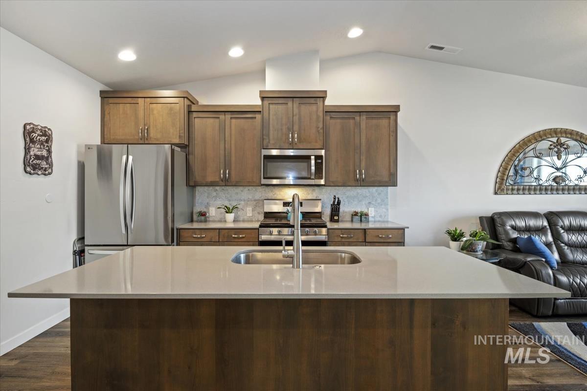 193 West Haniken Street Meridian, ID 83642 - Photo 7 of 27 Kitchen with tasteful backsplash, a kitchen island with sink, stainless steel appliances, dark wood-style floors, and light stone countertops