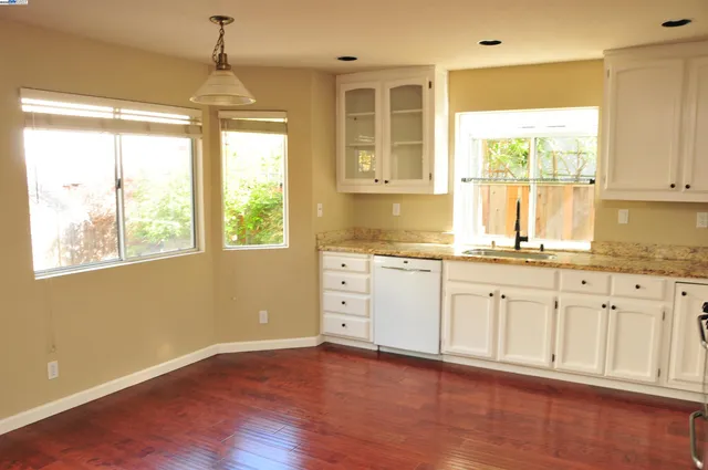a hall with kitchen island granite countertop white cabinets and wooden floor