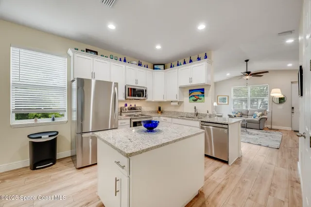 a kitchen with stainless steel appliances granite countertop a refrigerator a stove a sink dishwasher and white cabinets with wooden floor