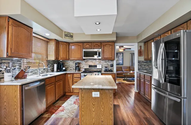 a kitchen with stainless steel appliances granite countertop a refrigerator a sink dishwasher a stove with wooden cabinets and floor