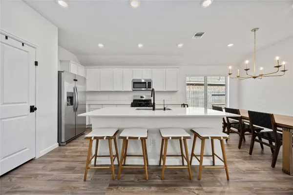 a kitchen with stainless steel appliances granite countertop a refrigerator a stove a sink a dining table and chairs with wooden floor